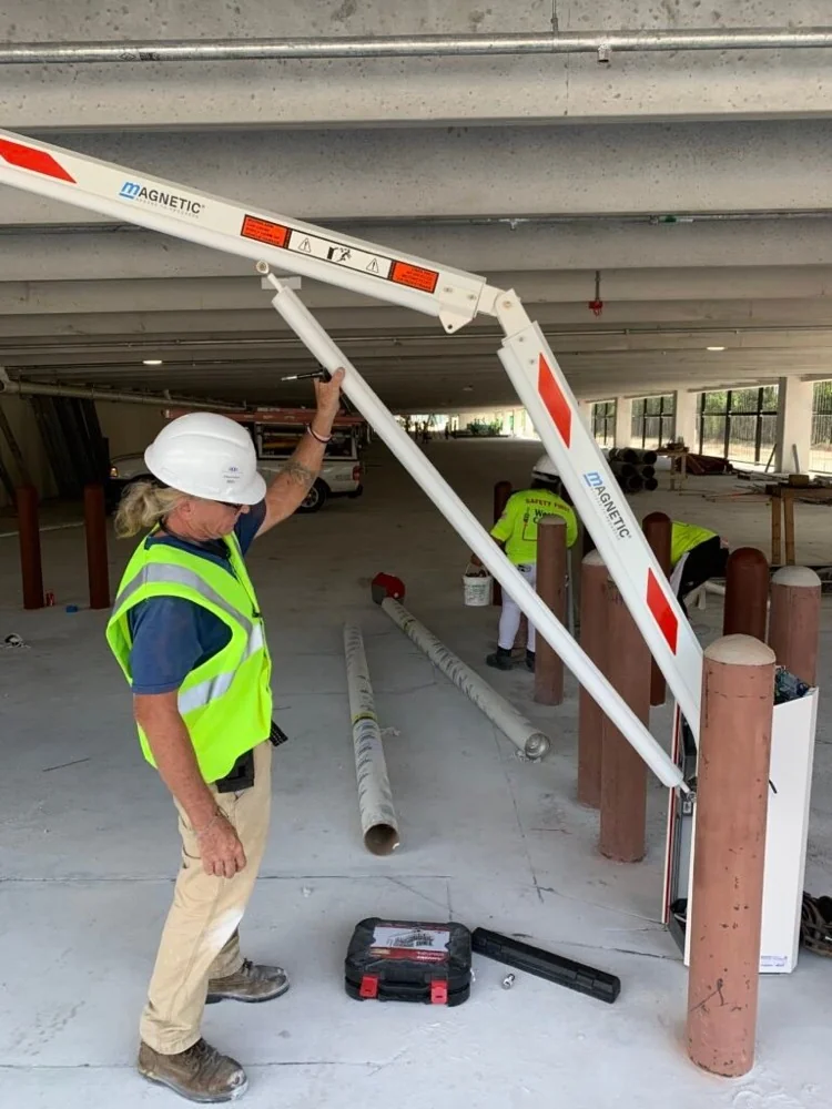 Technician in a hard hat fitting a barrier gate arm inside a parking garage